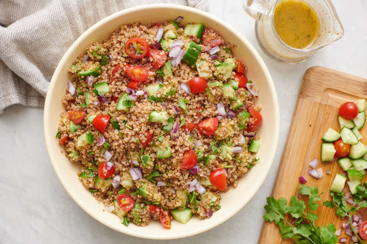 Quinoa avocado salad in a bowl with dressing and cutting board of more veggies nearby.